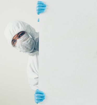 A doctor in mask, gloves and protective suit hiding and looking in white background . space for text. coronavirus